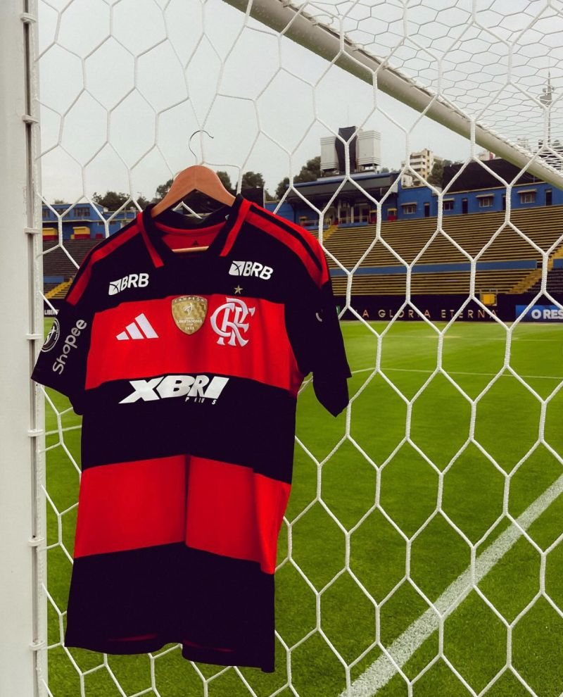Camisa do Flamengo com a marca XBRI pendurada na rede do gol de um estádio