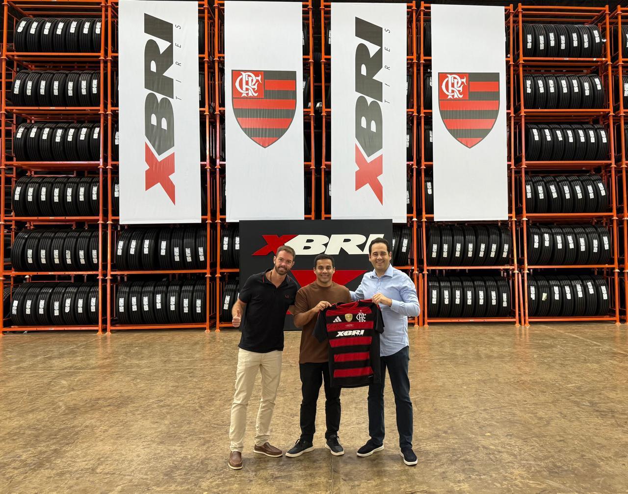 Representantes de XBRI y del Flamengo sostienen la camiseta rubro-negra con la marca XBRI en un depósito de neumáticos